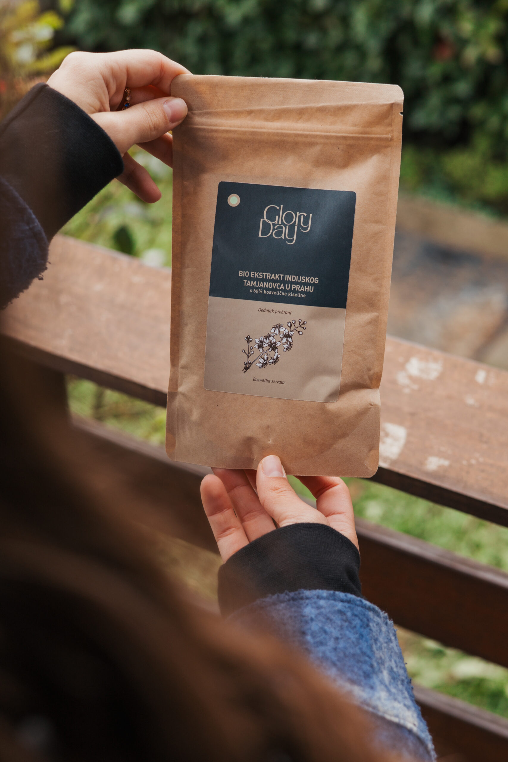 Osoba drži smeđu ambalažu s natpisom 'Glory Day Bio Ekstrakt Indijskog Tamjanovca u Prahu'.