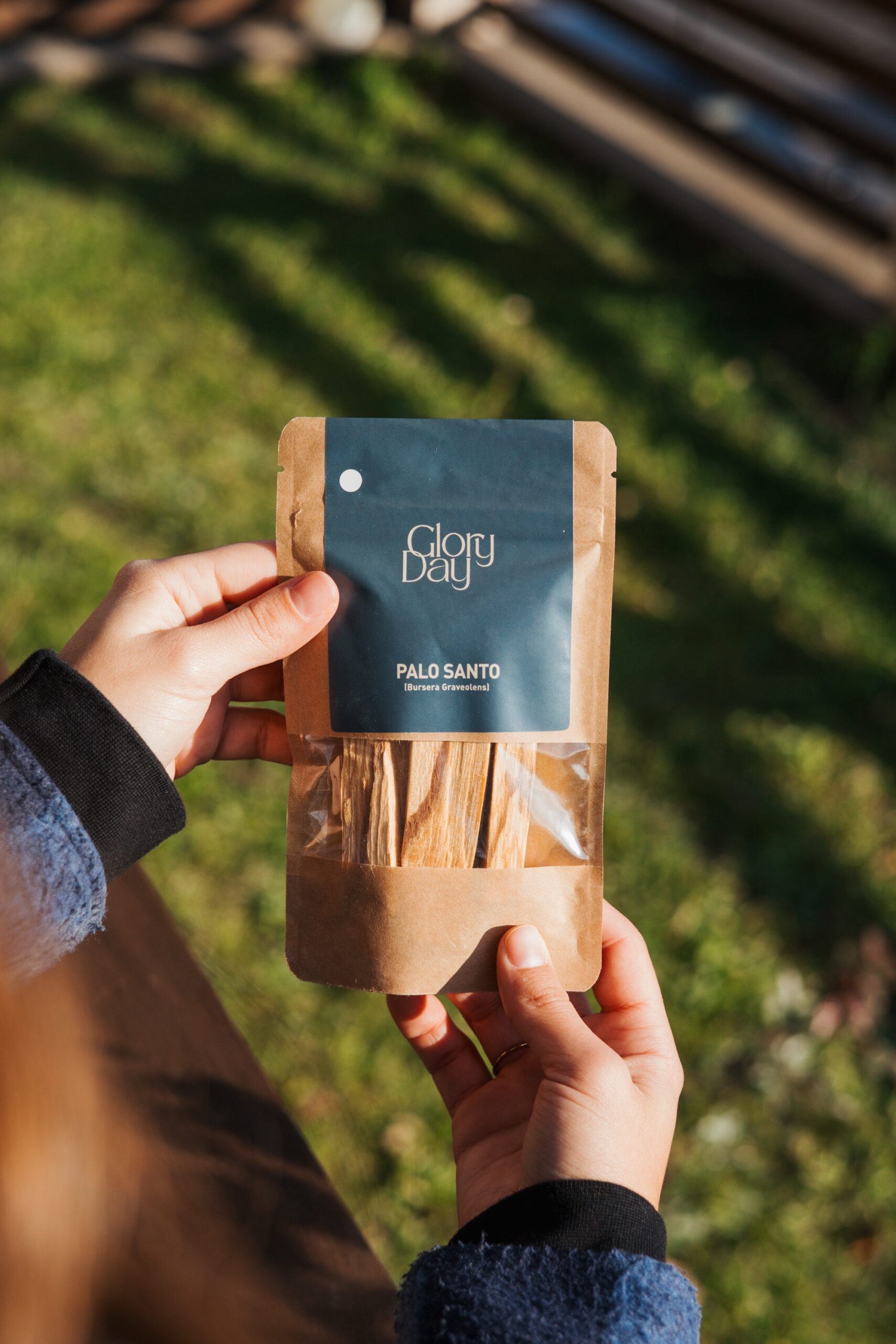 Osoba drži pakiranje Palo Santo štapića u prozirnoj smeđoj ambalaži s oznakom 'Glory Day' na otvorenom prostoru.