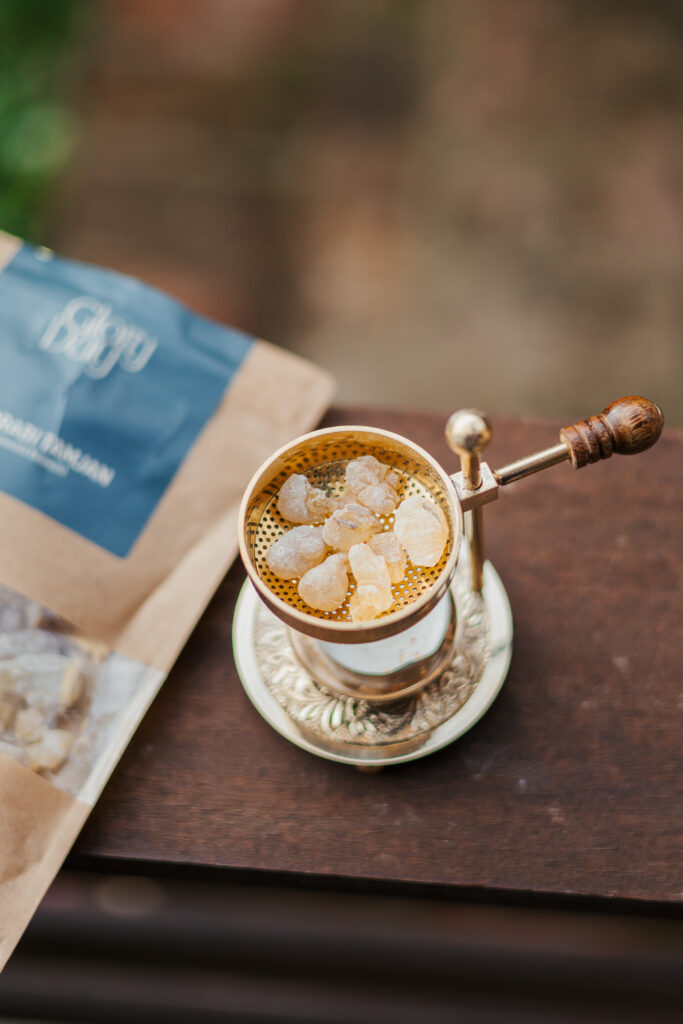 Tradicionalna kadilica s ručkom i metalnim detaljima, s grubim zrncima kave vidljivima na površini, postavljen pored pakiranja kave na drvenom stolu.