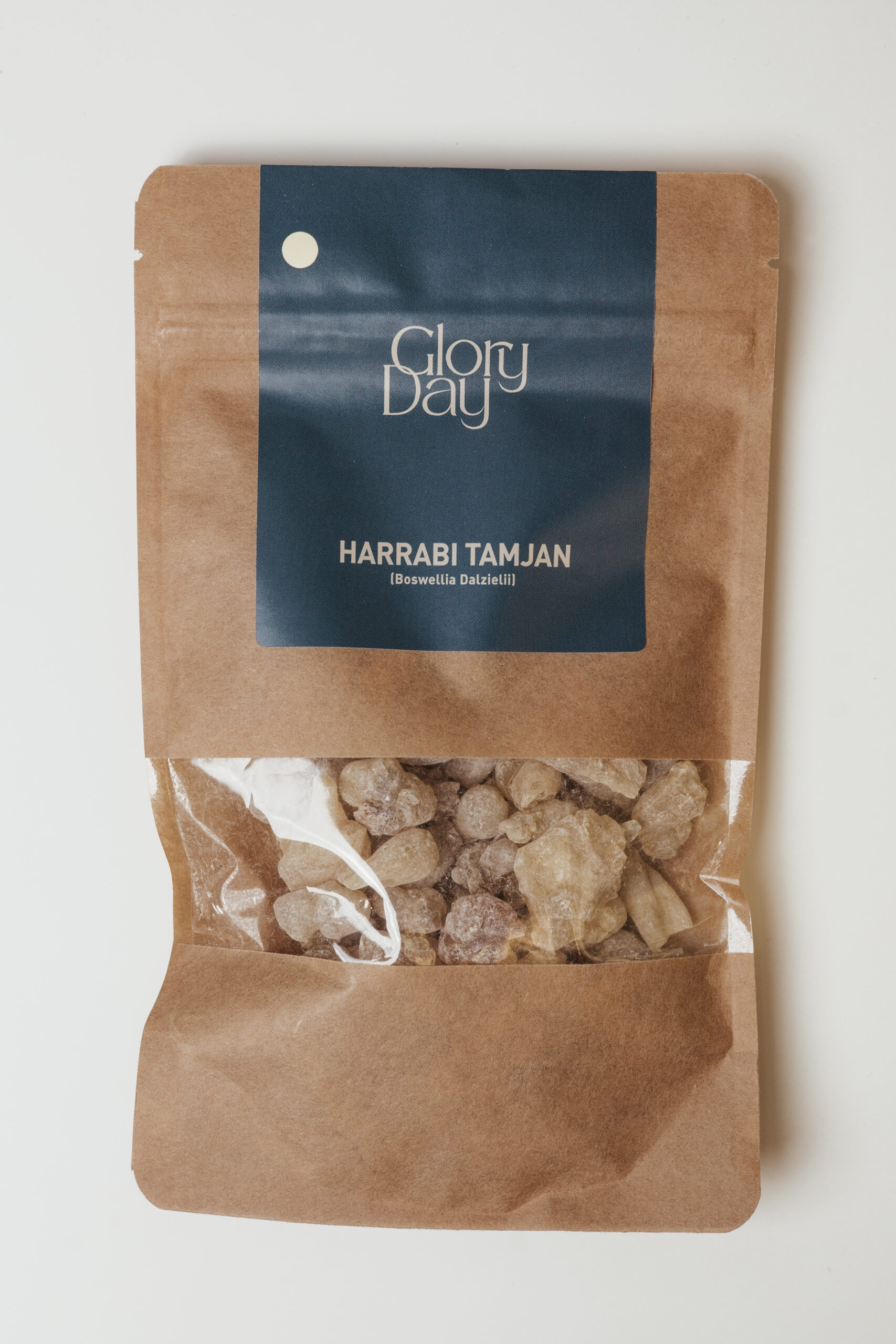 Pakiranje tamjana s natpisom "Glory Day Harrabi Tamjan (Boswellia Dalzielii)" na smeđoj papirnatoj vrećici s prozirnim dijelom kroz koji se vide komadići tamjana.