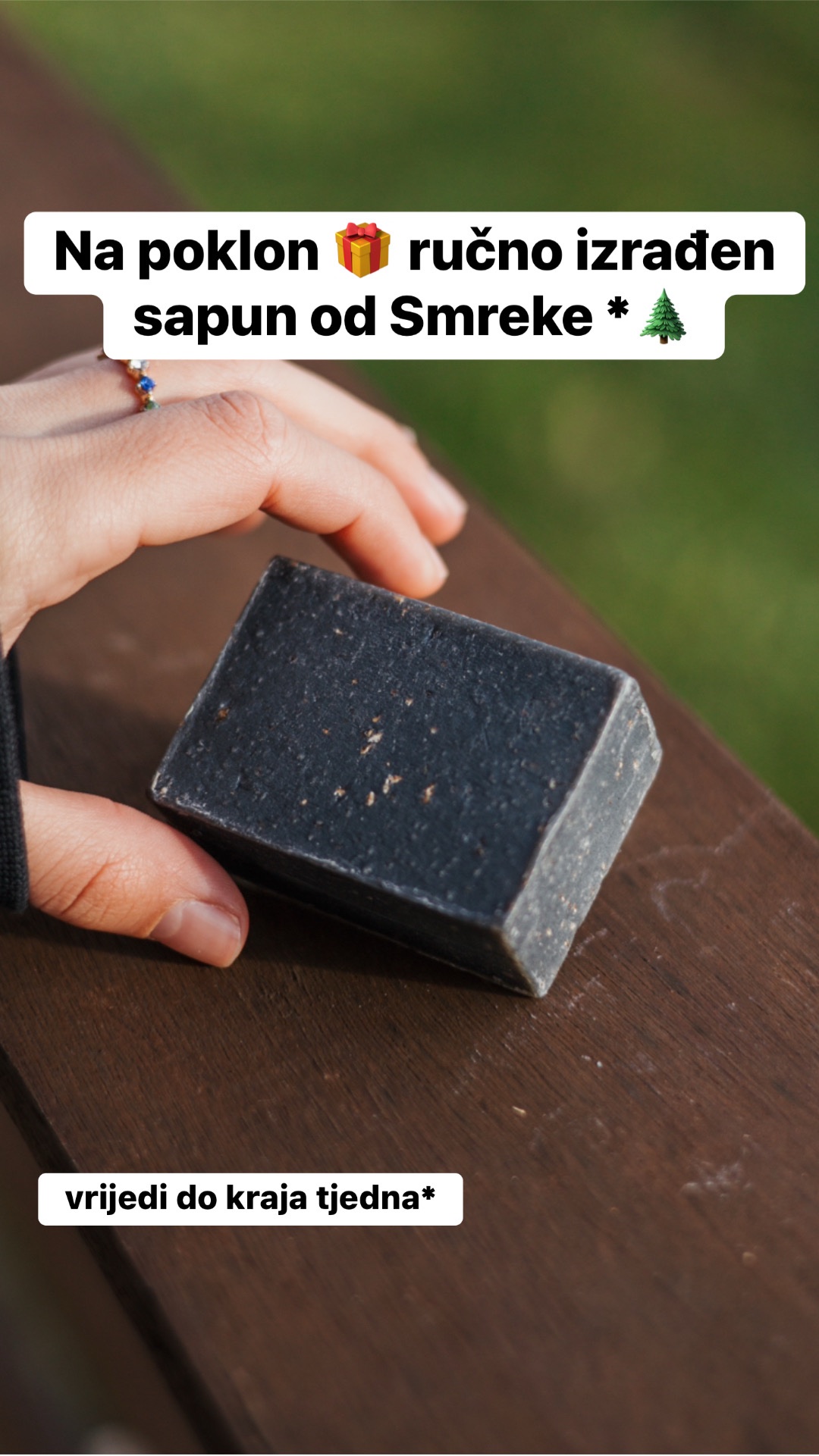 Ruka drži tamni sapun na drvenoj površini, s natpisom o ručno izrađenom sapunu od smreke brenda Glory day kao poklon te napomenom da ponuda vrijedi do kraja tjedna.
